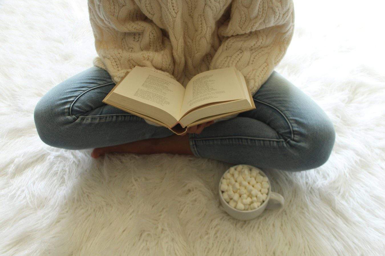 femmes avec jambes croisée sur un tapis lisant un livre